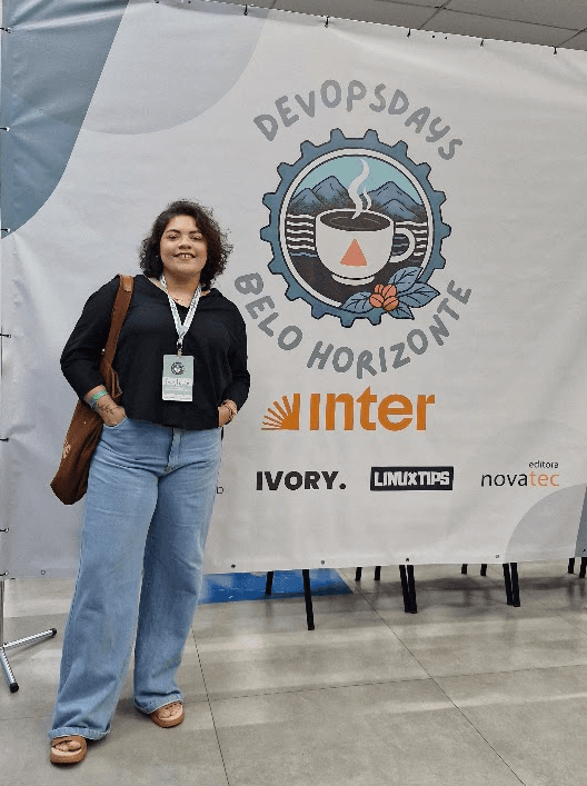 Ana Luiza Primo em frente ao banner do DevOps Days Belo Horizonte
